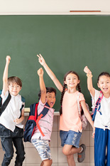 four elementary kids standing smiling with one arm  up, chalkboard in the background. 