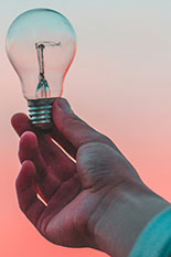 A hand holding a lightbulb against a sunset.