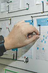A hand moves pins over a map attached to a bulletin board.
